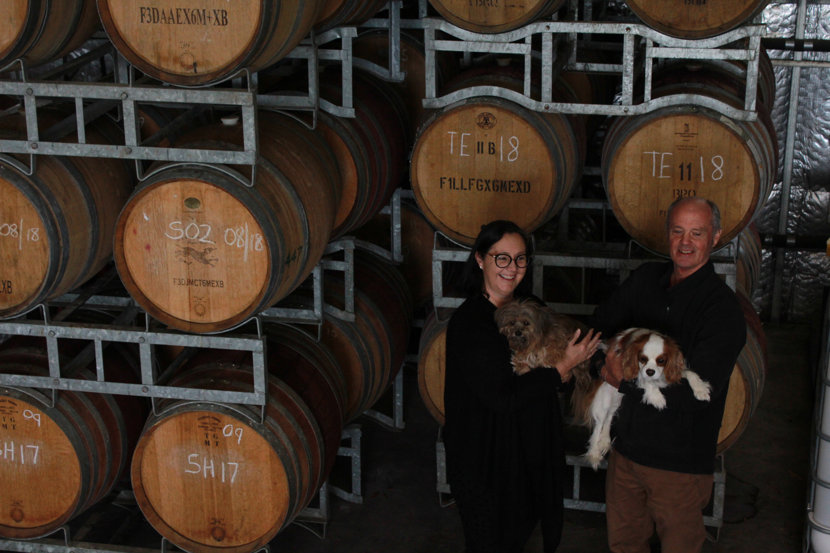A man and woman holding 2 dogs in the barrel room 